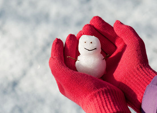 kleiner Schneemann gehalten von Händen in Handschuhen